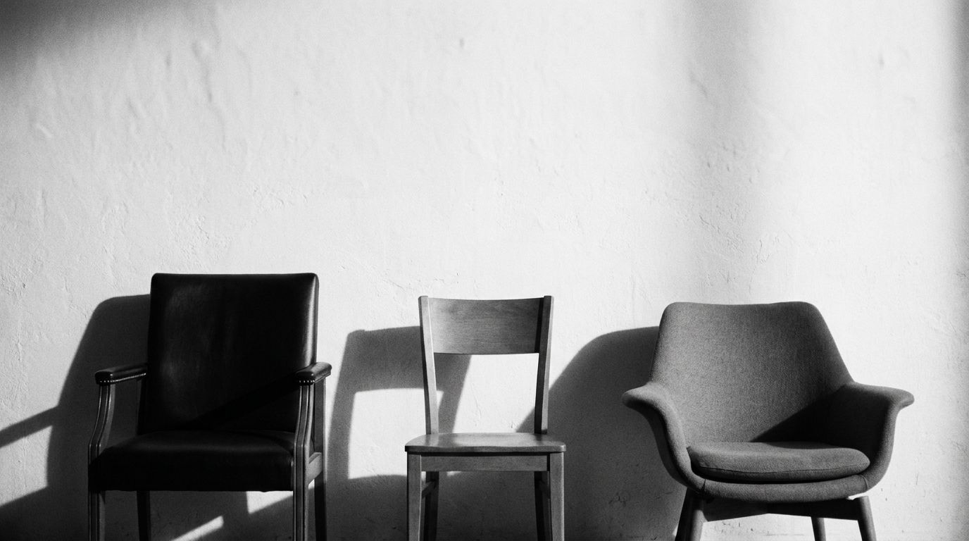 Three empty chairs of different kinds against a plaster wall, each casting its own shadow in low sunlight.